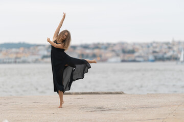 A woman in black dress dancing ballet on the pier