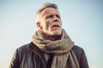 Group portrait photography of a man in his 50s grimacing and touching his throat due to strep throat wearing a charming scarf against a sky background 