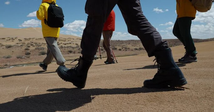 Travelers group go down slope along wild sand desert low angle shot close up. Hikers foots in trekking boots step at destination way, walking route exploration