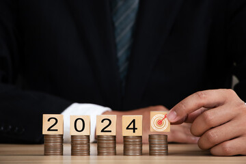 Business man hand holding  dartboard icon with Wooden cube 2024  place on top stack of coins. 2024...