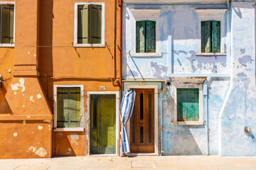 Facade of bright blue and orange painted houses with rustic green shutters and derelict paint.