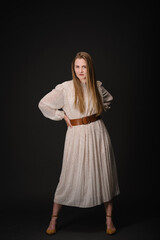 Young serious woman isolated on black wall with copy space. Beautiful girl with hands on waist looking at camera. Portrait of lady in long dress looks confident on black background. Photo.