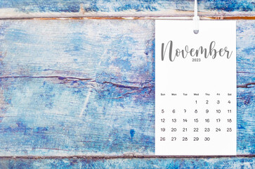 The November 2023 calendar page hanged with white rope  on old blue wooden background.