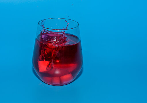 Izolowana szklanka z czerwonym zimnym napojem, wrzucać kostki lodu