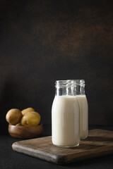 Vegan potato milk in bottles and potato on brown background. Plant based milk replacer and lactose free. Close up. Vertical.
