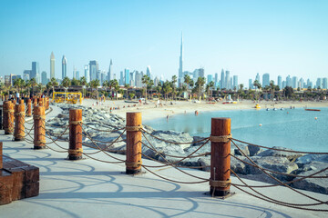 The wooden pillars of Dubai's La Mer beach, people are relaxing, the skyscrapers of the city are...