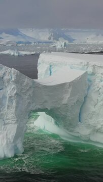 Vertical video huge snowy white iceberg with an arch in Antarctic Ocean. Snowy mountains of Antarctic Ocean create bewitching picture in Antarctica.