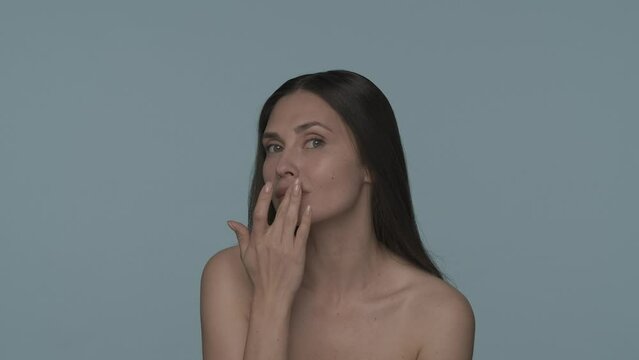 A woman touches her lips while moisturizing them on a blue background close up. A woman applies lip balm, a cosmetic product for natural hydration, healing of dry and chapped lips. Slow motion. HDR