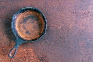 Old rusty round cast iron frying pan on old rusty background, view from above
