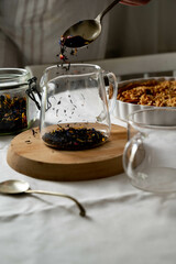 Black tea. Pouring dried black tea in glass teapot. Dark and moody.