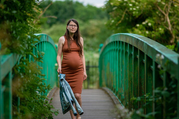 Caucasian Young Pregnant woman Tummy belly summer green  bridge touching stomach field expecting baby relaxing outside nature park Beautiful magic glasses brown Tight dress Bridge River Lee Navigation