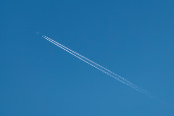 A plane crosses the blue sky diagonally leaving behind a double white trail