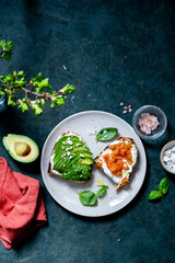 Avocado and salmon toasts with sourdough bread, sliced avocado, cream cheese and seeds, top view.