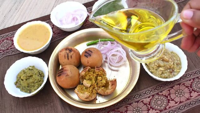 Litti in white plate with tomato, brinjal, potato, pointed gaurd and coriander chutney or chokha and ghee. It is popular in Bihar, Uttar Pradesh and Jharkhand.