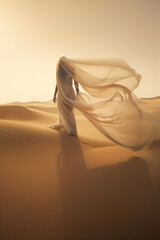 Woman in a long dress walking in the desert with flowing fabric in the wind