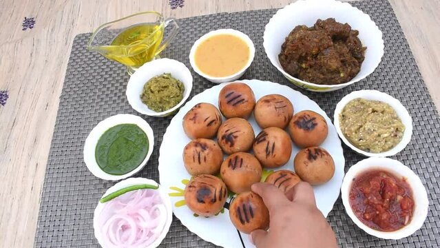 Litti in white plate with tomato, brinjal, potato, pointed gaurd and coriander chutney or chokha and ghee. It is popular in Bihar, Uttar Pradesh and Jharkhand.
