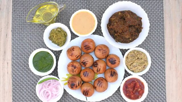 Litti in white plate with tomato, brinjal, potato, pointed gaurd and coriander chutney or chokha and ghee. It is popular in Bihar, Uttar Pradesh and Jharkhand.