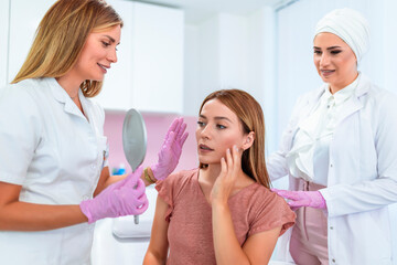 Doctor and nurse examine the patient before the aesthetic procedures. The patient is looking at herself and telling them what she wants to change.