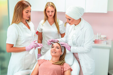 Obraz na płótnie Canvas Three beautiful doctors and cosmeticians doing multiple facial treatments on a young woman's face