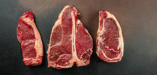 Meat Steaks T-bone between knife, on black stone background. Raw beef meat. Long banner format. top...