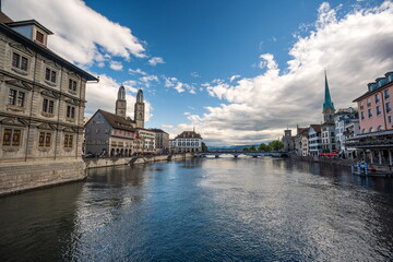 Fototapeta na wymiar 03-08-2023 Zurich city Switzerland. Bridge side view of the famous Grossmunster and Fraumunster cathedral towers on either side of the Limmat river. Sunny summer day, blue sky and puffy white clouds