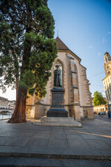 Fototapeta na wymiar 03-08-2023 Zurich city Switzerland. Wide-angle view of Wasserkirche Zürich or Water Church. Setting sun in the background, large tree next to bronze statue