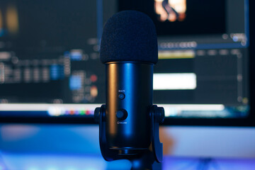 Videomaker desk, close up on a microphone with a blurred monitor in the background.