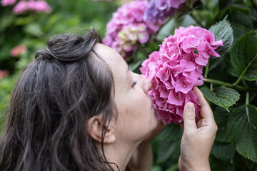 A woman inhales the scent of pink hydrangea, the concept of unity with nature