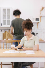 woman pays electricity rent bills, man cooks lunch. African American young married person kitchen...