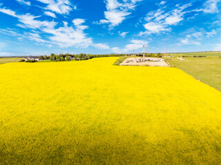 Aerial blooming canola field overlooking an oil and gas drilling rig next to a rural property near the Calgary city limits in Rocky County Alberta Canada.