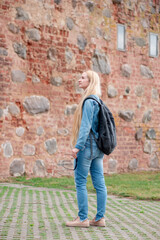 Girl tourist with a backpack in jeans clothes on the background of a brick building.