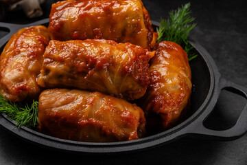 The concept of Ukrainian cuisine. Cabbage rolls with rice, with tomato sauce lie on a pan, on a black background.