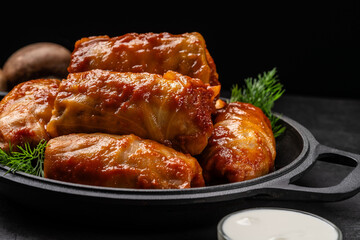 The concept of Ukrainian cuisine. Cabbage rolls with rice, with tomato sauce lie on a pan, on a black background.
