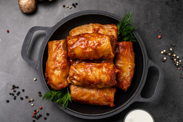The concept of Ukrainian cuisine. Cabbage rolls with rice, with tomato sauce lie on a pan, on a black background.