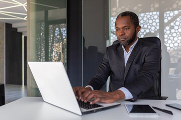 Fototapeta na wymiar Serious mature businessman working on laptop inside office at workplace, african american boss thoughtful in business suit, successful experienced investor banker.