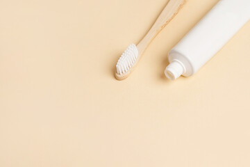 Blank white tube of toothpaste and wood brush on beige background, copy space