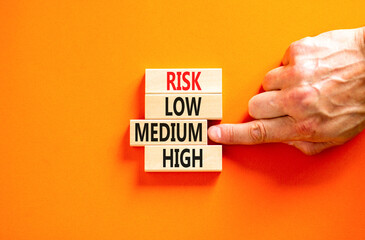 Time to medium risk symbol. Concept word Risk low medium high on wooden block. Businessman hand. Beautiful orange table orange background. Business time to medium risk concept. Copy space.