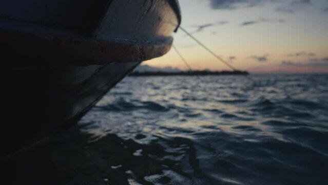 Beautiful sea water splashing on fishing boat. Ripples of ocean and fishermans vessel at sunset. Seascape with grey waves under pink sky. Blue color Island coast in twilight . Sunrise in open sea.