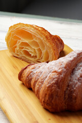 Freshly baked croissant with powdered sugar on wooden board