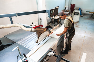 Young carpenter cutting a piece of wood in using a circular saw in furniture factory