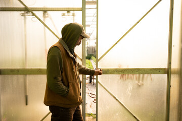 A middle aged farmer opens the door to his greenhouse in the early morning light.