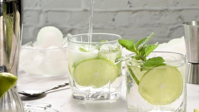 Mint mojito is the perfect non-alcoholic recipe. A glass with ice, lime and mint is filled with tonic. Close-up. This is one part of a series of vertical videos. Super slow motion