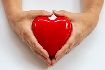 Hands of elderly woman holding red heart on white background. Concept of love, valentine's day, health. Greeting card.