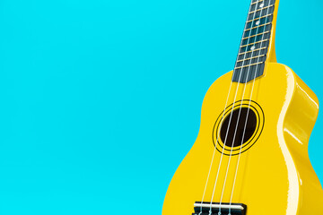 Close-up photo of ukulele with copy space. Yellow colored wooden ukulele guitar on the turquoise...