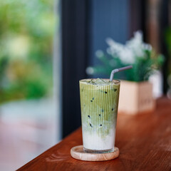 Iced Tea. A glass of iced matcha green tea latte with soft focus, on wooden table and by the...