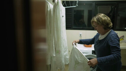 Candid senior woman putting sheets to dry at laudry room rack. Person drying clothes