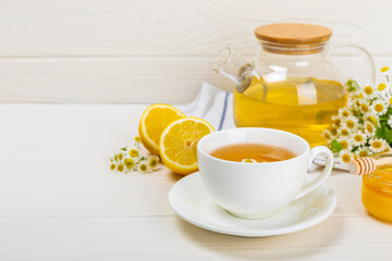 Chamomile tea on a white table. Delicious tonic, soothing and relaxing chamomile tea with chamomile flowers, honey and lemon. Herbal tea for immunity. Close-up.Place for text.Copy space.