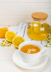 Chamomile tea on a white table. Delicious tonic, soothing and relaxing chamomile tea with chamomile flowers, honey and lemon. Herbal tea for immunity. Close-up.Place for text.Copy space.