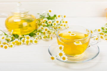 Chamomile tea on a white table. Delicious tonic, soothing and relaxing chamomile tea with chamomile flowers, honey and lemon. Herbal tea for immunity. Close-up.Place for text.Copy space.