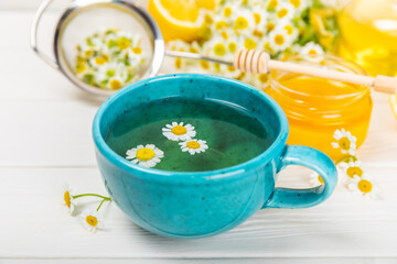 Chamomile tea on a white table. Delicious tonic, soothing and relaxing chamomile tea with chamomile flowers, honey and lemon. Herbal tea for immunity. Close-up.Place for text.Copy space.